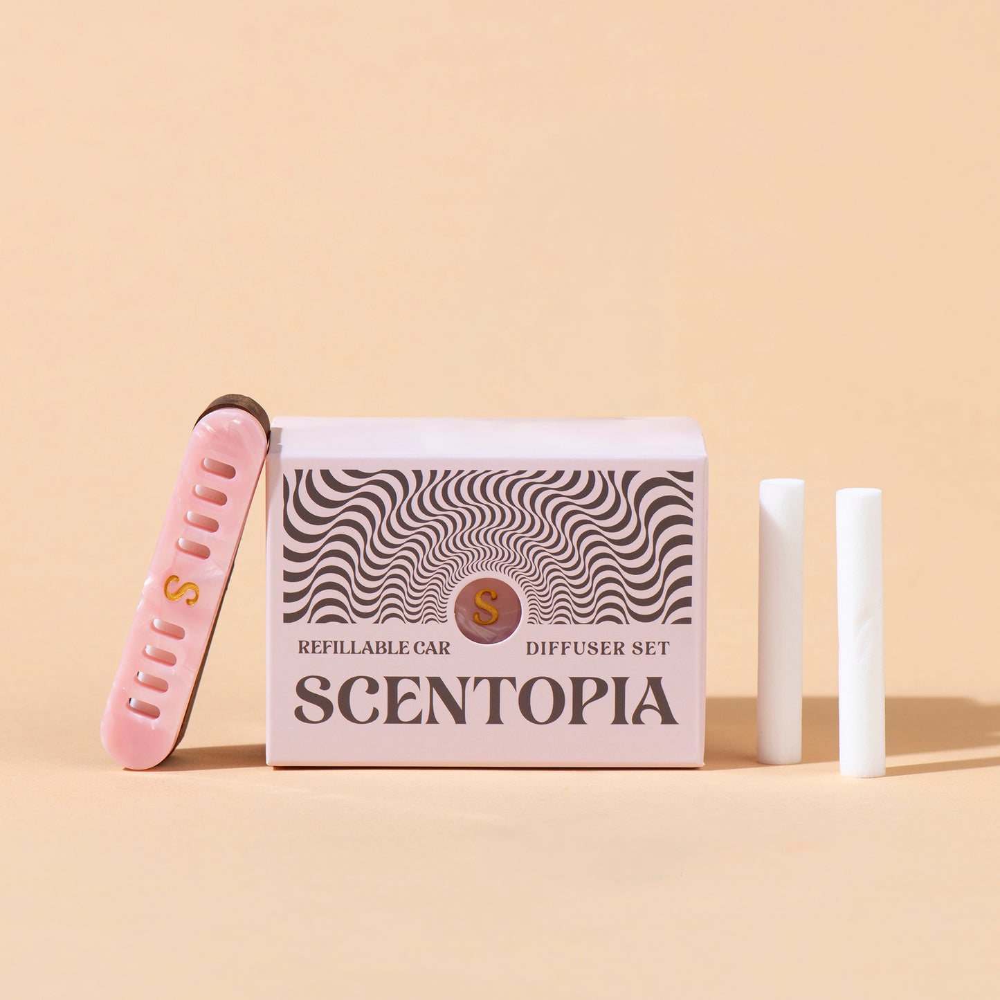 Scentopia Petal refillable car diffuser set featuring a pink box with black wavy patterns, a pink nail file, and two white car diffuser rods on a beige background.