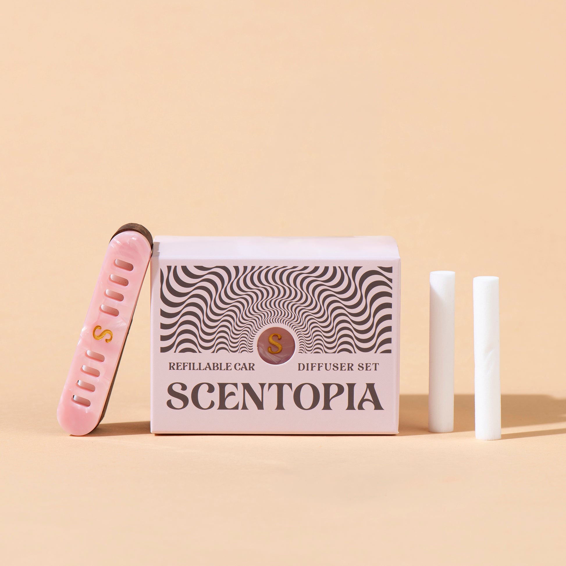Scentopia Petal refillable car diffuser set featuring a pink box with black wavy patterns, a pink nail file, and two white car diffuser rods on a beige background.