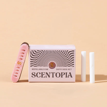 Scentopia Petal refillable car diffuser set featuring a pink box with black wavy patterns, a pink nail file, and two white car diffuser rods on a beige background.