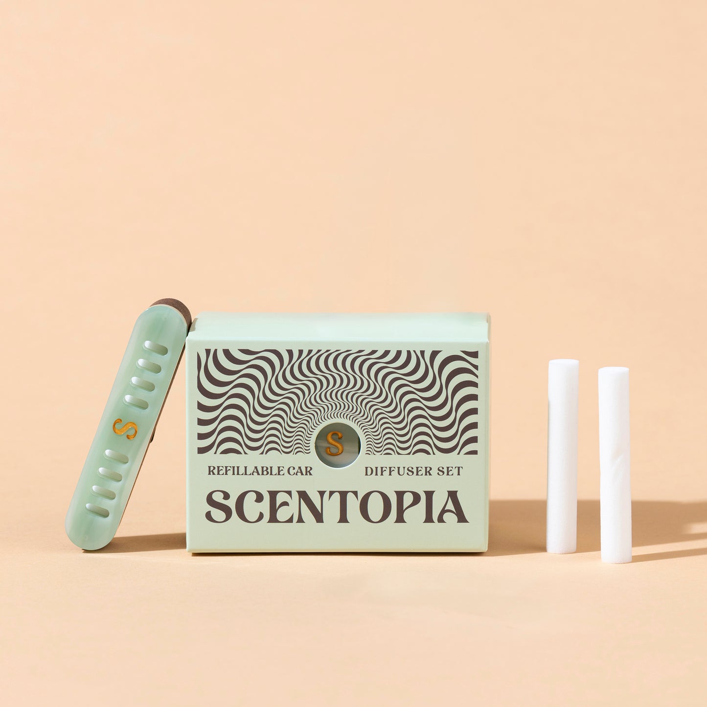 Scentopia refillable car diffuser set featuring a jade green box with black wavy patterns, a jade green diffuser device leaning against it, and two white cartridges on a warm beige background.