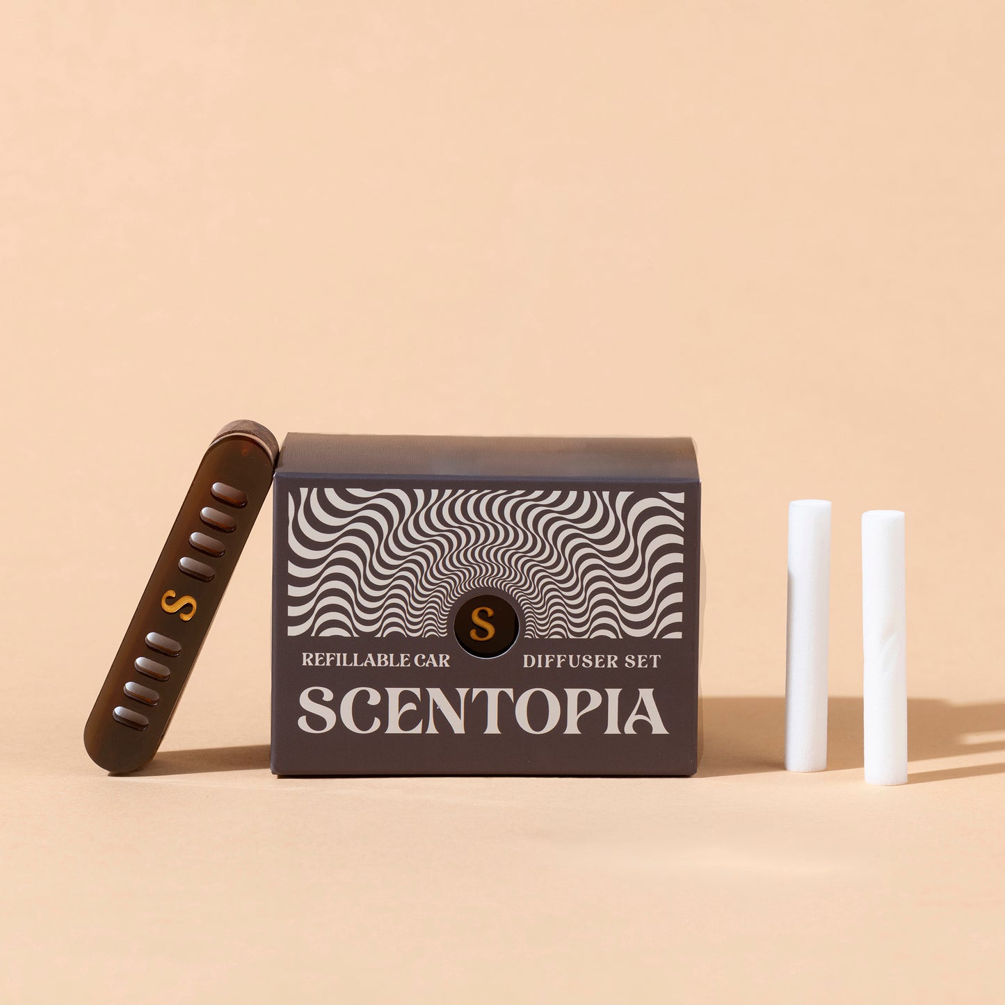 Scentopia refillable car diffuser set with a dark brown box featuring a black and white wavy pattern, a brown diffuser device with a gold 'S' logo, and two white cartridges on a beige background.