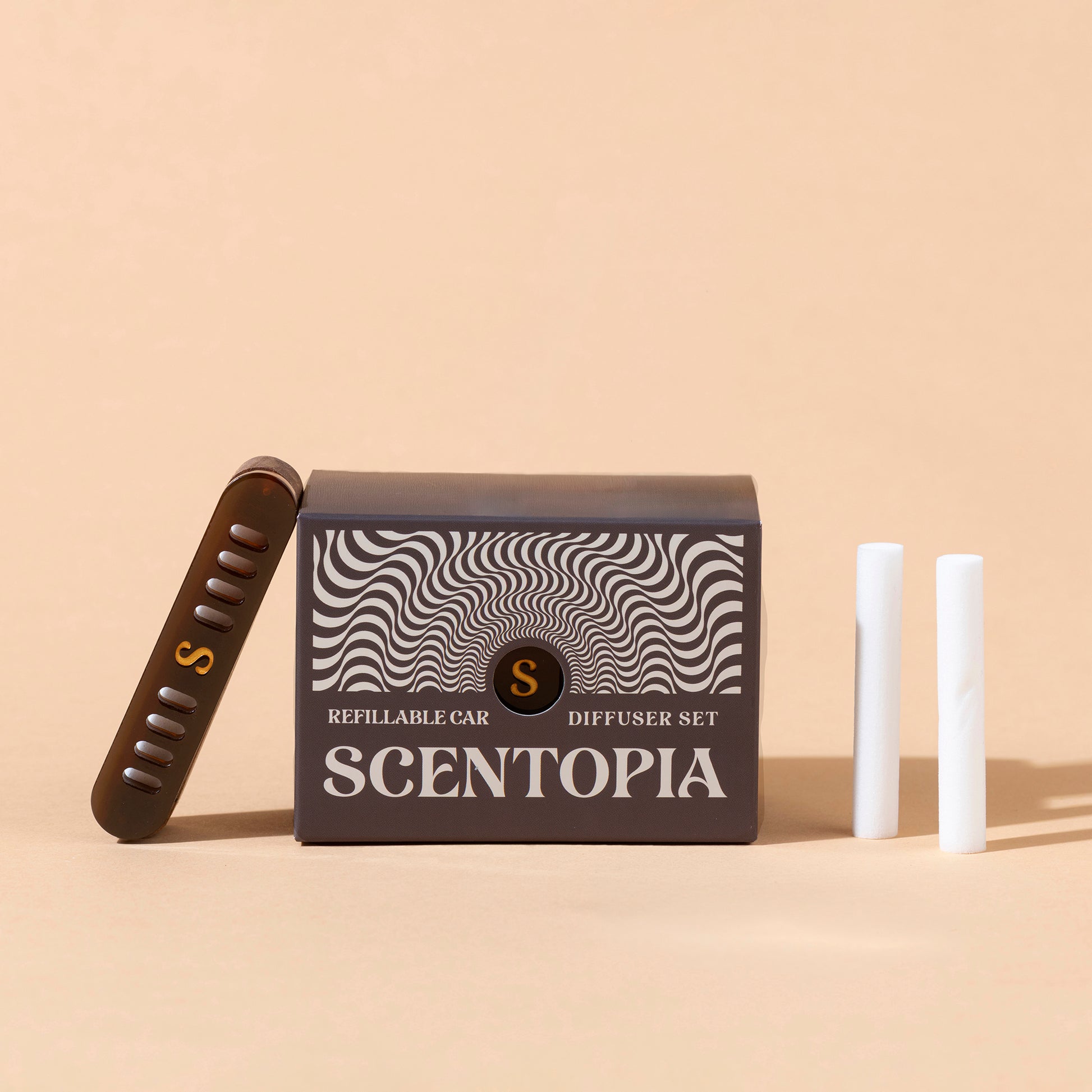 Scentopia refillable car diffuser set with a dark brown box featuring a black and white wavy pattern, a brown diffuser device with a gold 'S' logo, and two white cartridges on a beige background.