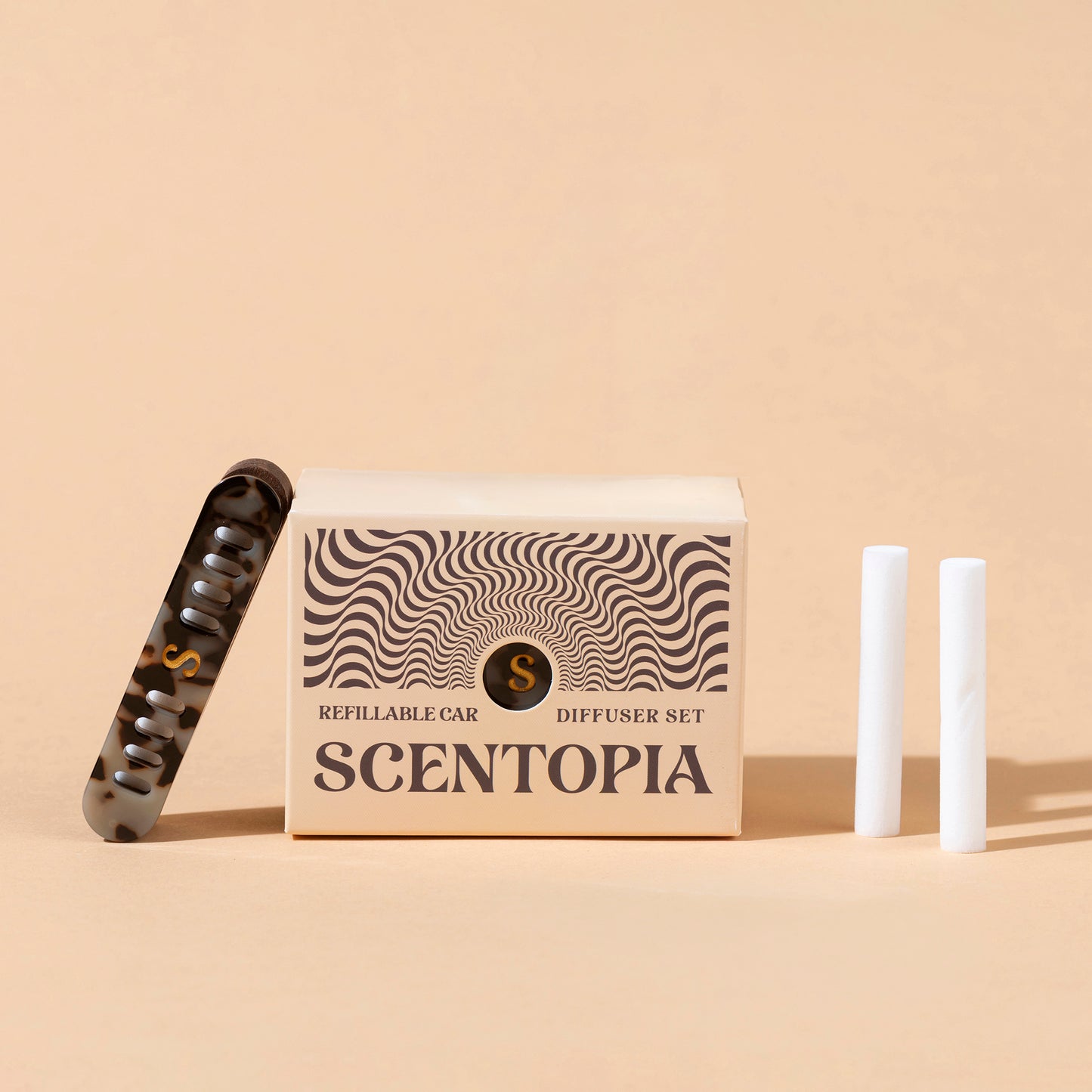 Scentopia refillable car diffuser set featuring a beige patterned box, a tortoiseshell aceate car diffuser, and two white refil rods on a beige background.