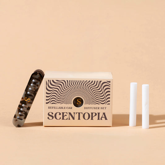 Scentopia refillable car diffuser set featuring a beige patterned box, a tortoiseshell aceate car diffuser, and two white refil rods on a beige background.