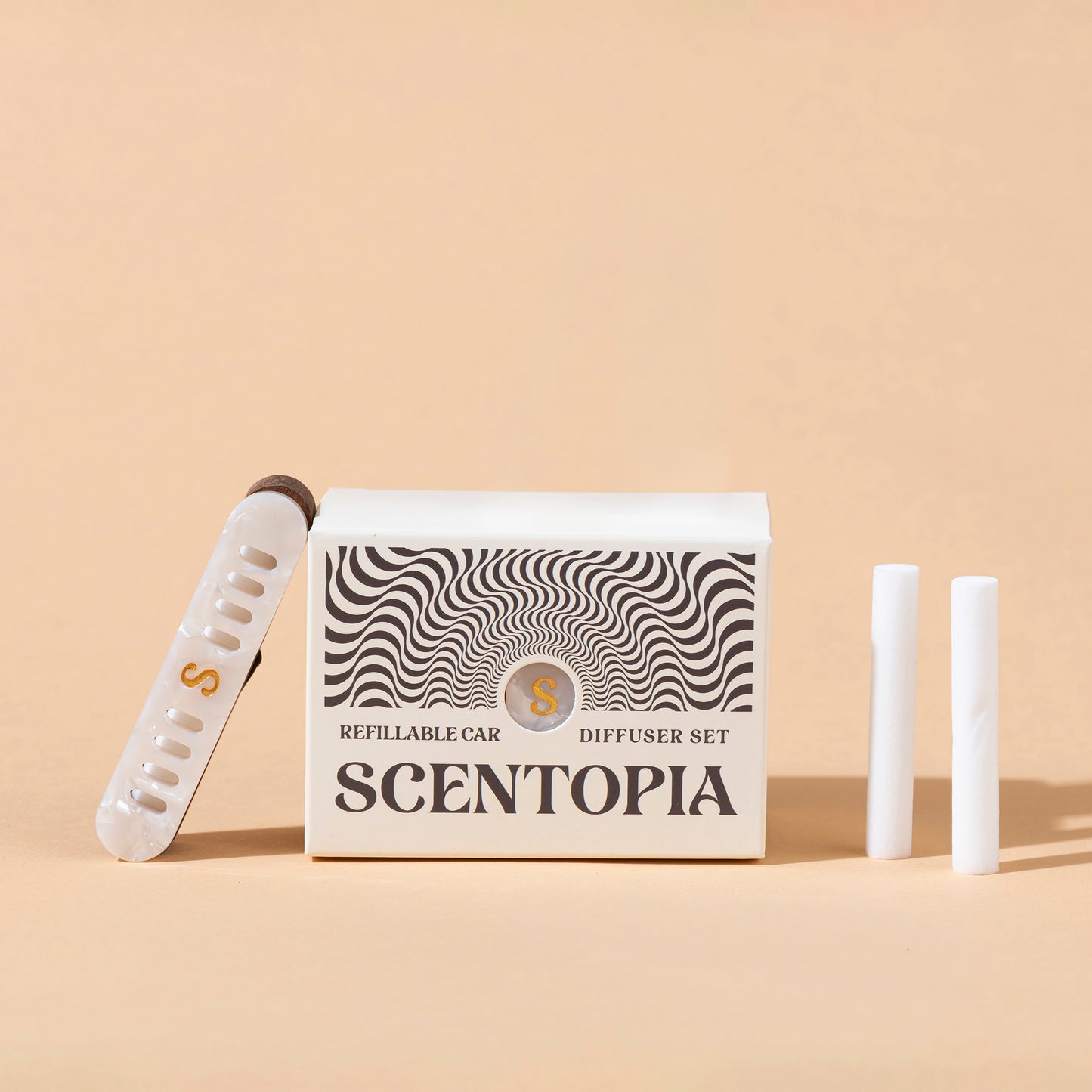 Scentopia refillable car diffuser set with a white box featuring black wavy patterns, a pearl car diffuser with a gold S, and two white refill rods on a beige background.