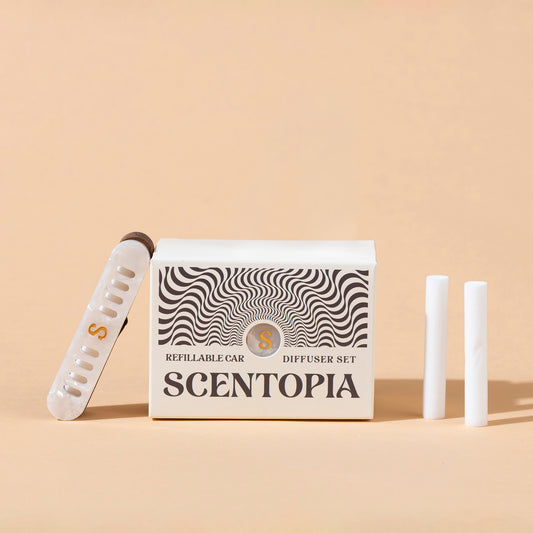 Scentopia refillable car diffuser set with a white box featuring black wavy patterns, a pearl car diffuser with a gold S, and two white refill rods on a beige background.