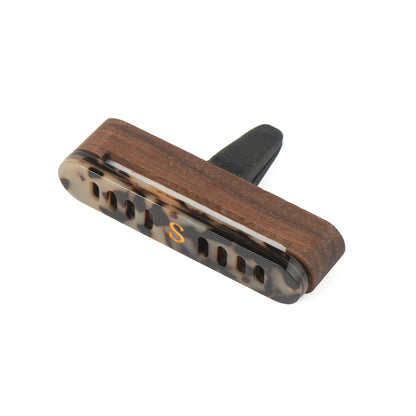 A Scentopia car diffuser in tortoiseshell acetate in brown, black, and beige, featuring a gold-colored 'S' monogram n the front. With a wooden case, set against a plain white background.
