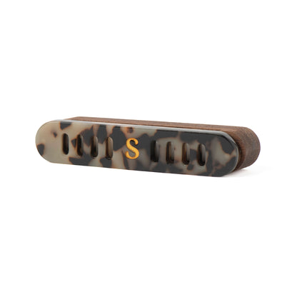 A Scentopia car diffuser in tortoiseshell acetate in brown, black, and beige, featuring a gold-colored 'S' monogram on the front, set against a plain white background.