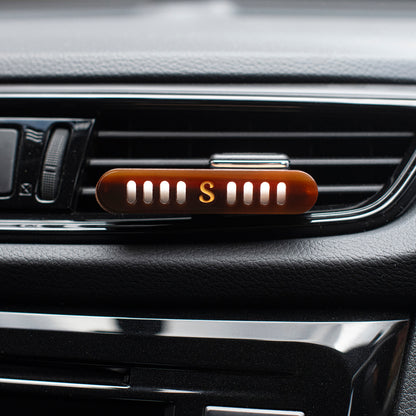 Scentopia car air freshener diffuser with an espresso aceate lid showing a gold letter 'S', clipped onto a car's air vent.