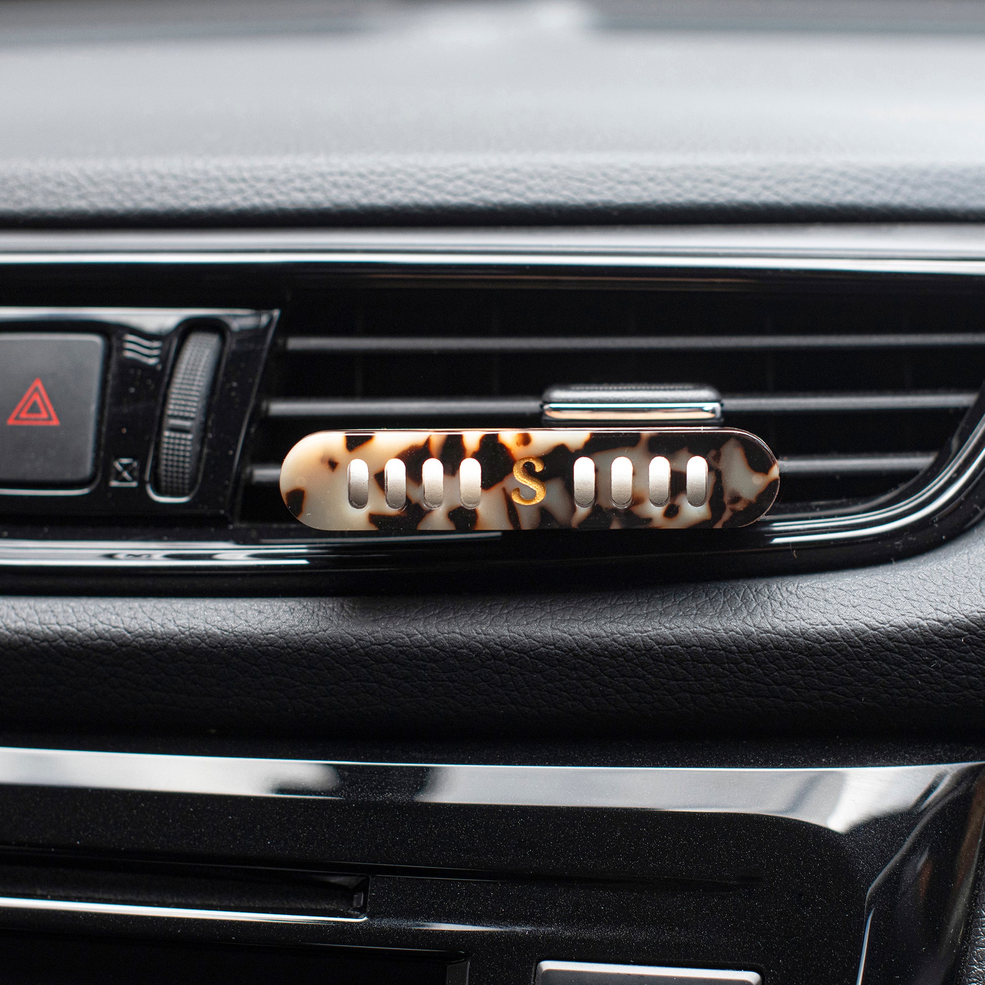 A Scentopia  tortoiseshell acetate car air diffuser clip mounted on a car dashboard air vent.