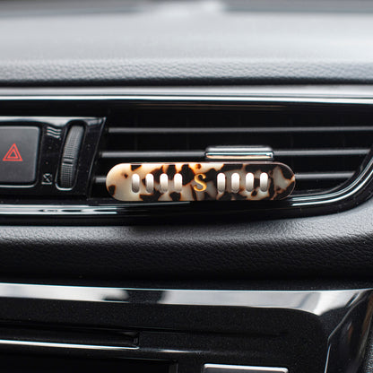 A Scentopia  tortoiseshell acetate car air diffuser clip mounted on a car dashboard air vent.