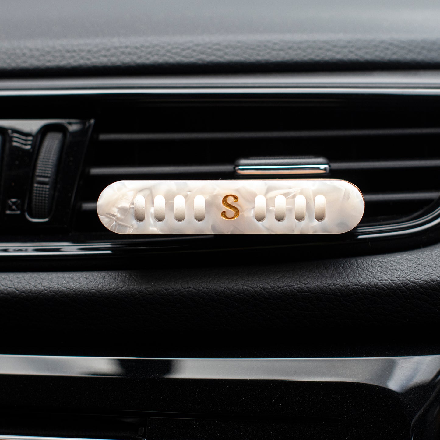 A close-up of a Scentopia car diffuser with a white mother-of-pearl oval clip featuring a gold letter 'S' in the center.
