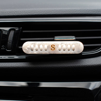 A close-up of a Scentopia car diffuser with a white mother-of-pearl oval clip featuring a gold letter 'S' in the center.