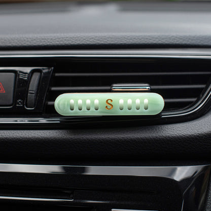 A  Scentopia light jade green car vent diffuser with a small gold letter 'S' in the center, clipped onto a black car air vent.