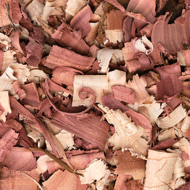 A close-up of curled and shredded cedarwood shavings in muted pinkish-brown and cream tones, filling the entire frame.