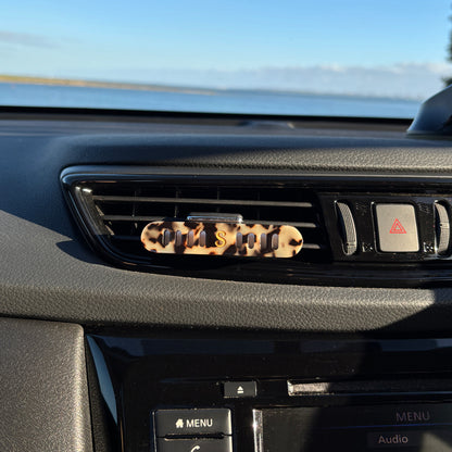 A Scentopia car air freshener diffuser  in  tortoiseshell acetate, placed on a car's air vent.