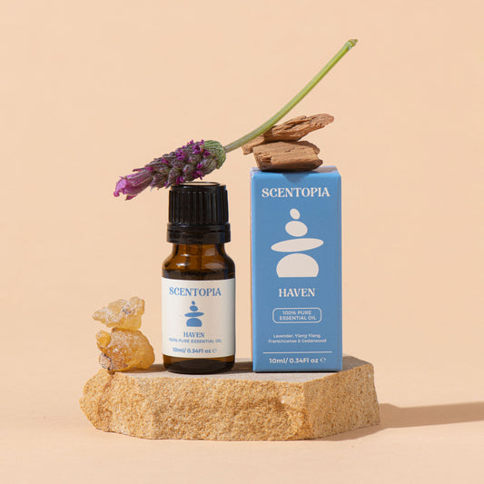 Scentopia Haven 100% pure essential oil bottle and blue box packaging, styled on a stone pedestal with lavender and wood against a warm beige background.